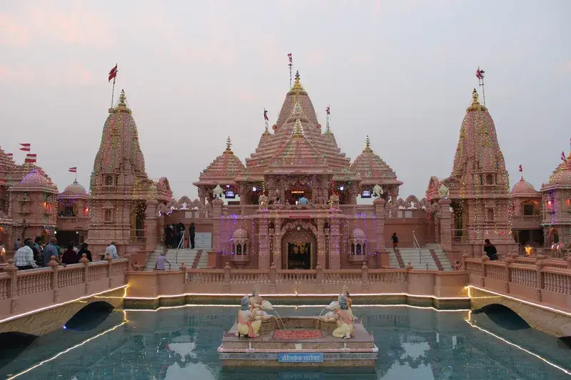The spires of Nilkanth Dham, Poicha, across the temple lake at dusk